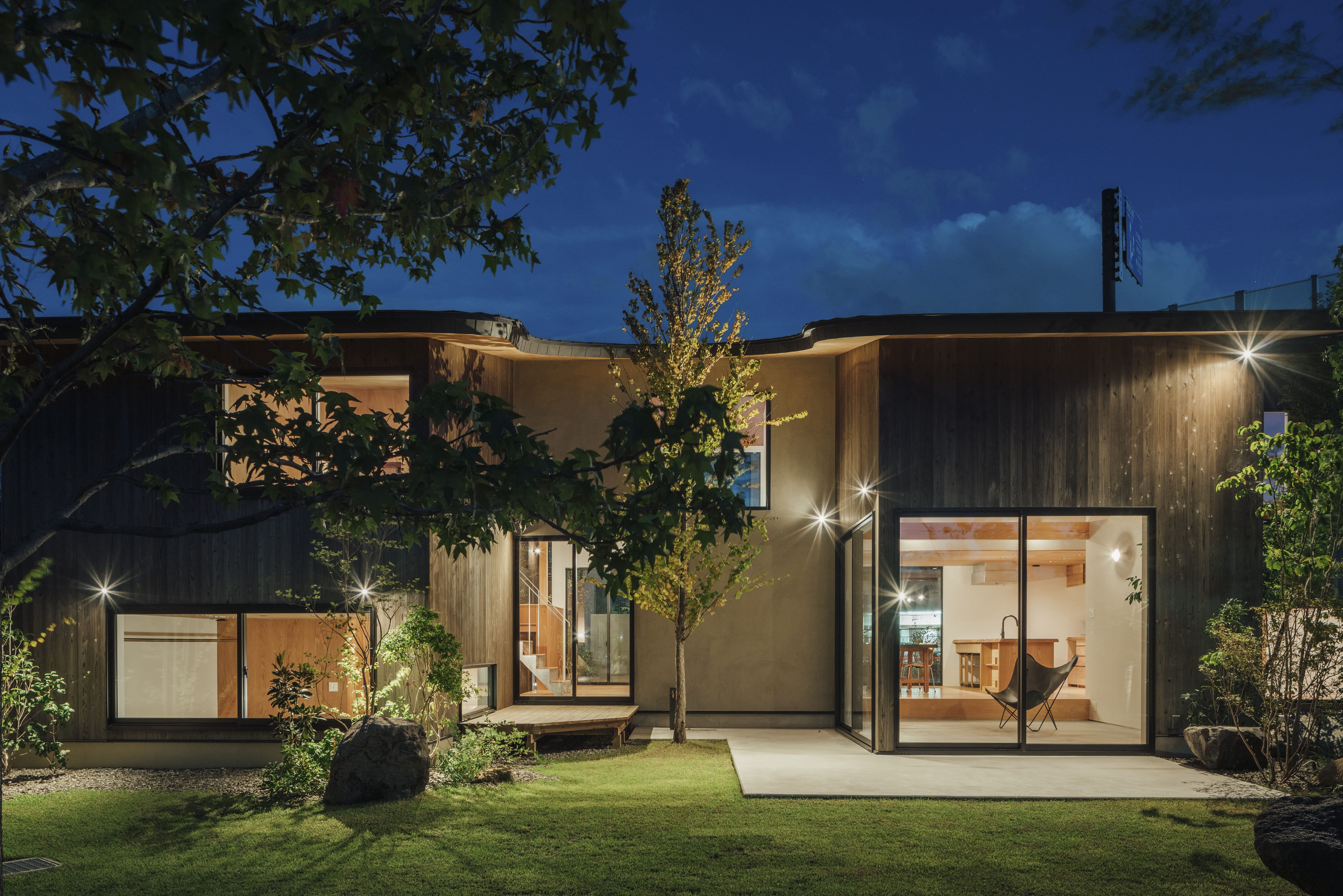 夜の庭、スポットライトに照らされる焼杉の外壁と暖かいリビング